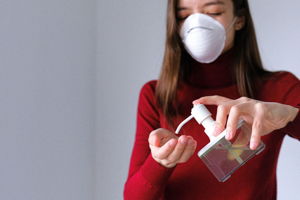 Nell'immagine una ragazza indossa una mascherina FFp2 mentre sanifica le mani utilizzando dell'alcol versato da un dispenser